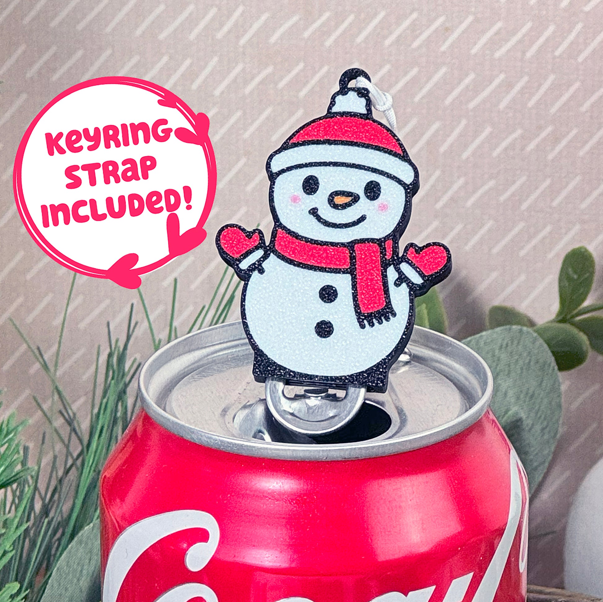 Snowman Tab Buddy with keyring strap included on a Coca-Cola can with plants in the background