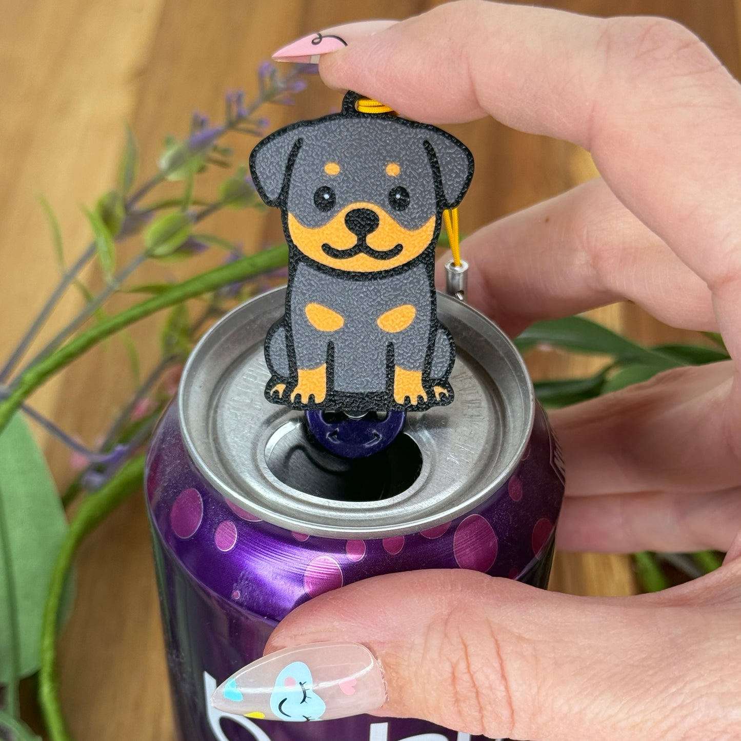 A person with long fingernails rests a finger atop a Rottweiler design Tab Buddy after using it to open a purple can of sparkling water.