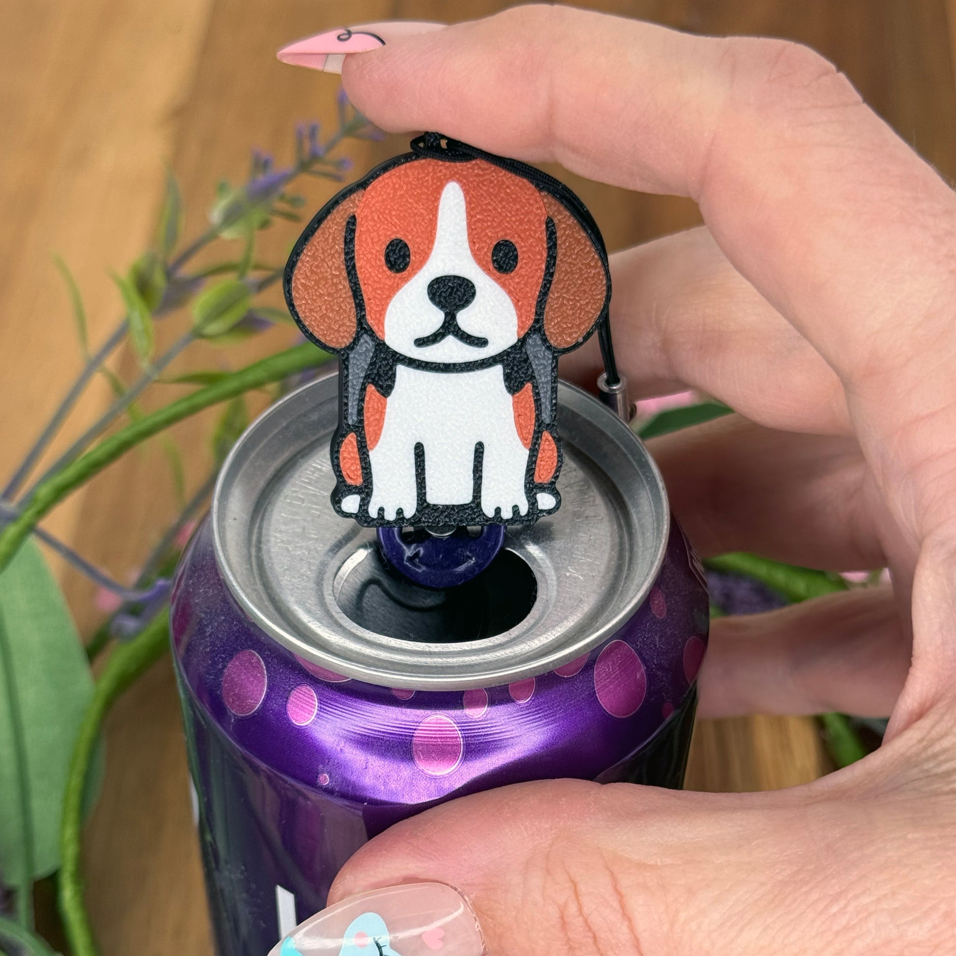 A person with long fingernails rests a finger atop a Beagle design Tab Buddy after using it to open a purple can of sparkling water.