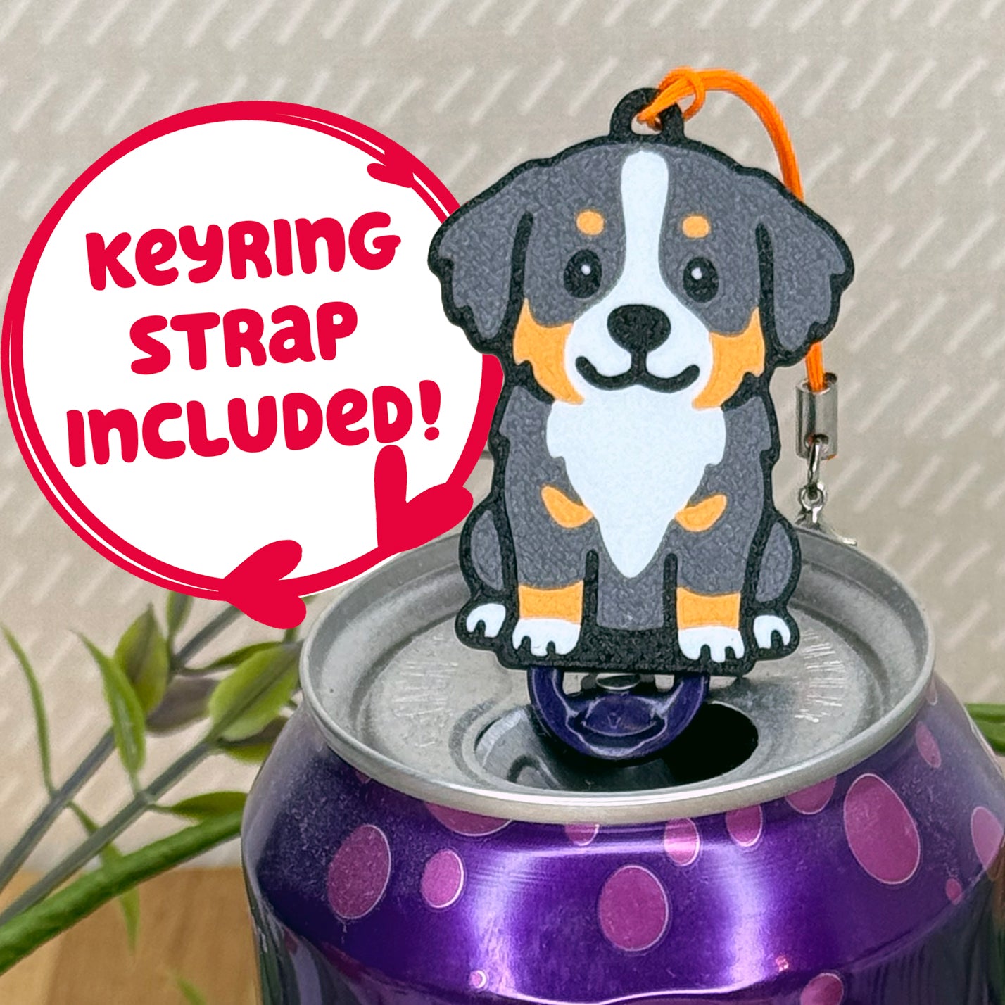 A cute Bernese Mountain Dog design Tab Buddy rests atop an open can of sparkling water. Text bubble reads, "Keyring Strap Included!"