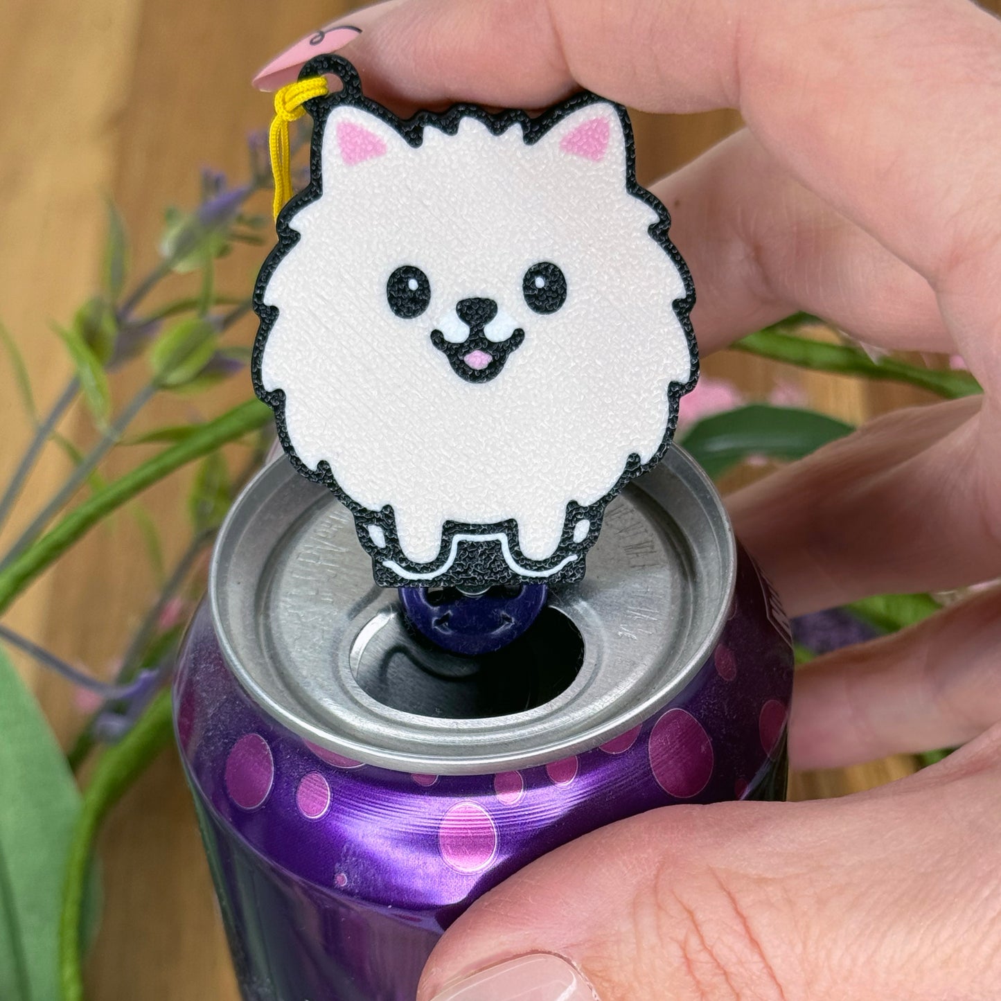 A person with long fingernails rests a finger atop a Pomeranian design Tab Buddy after using it to open a purple can of sparkling water.