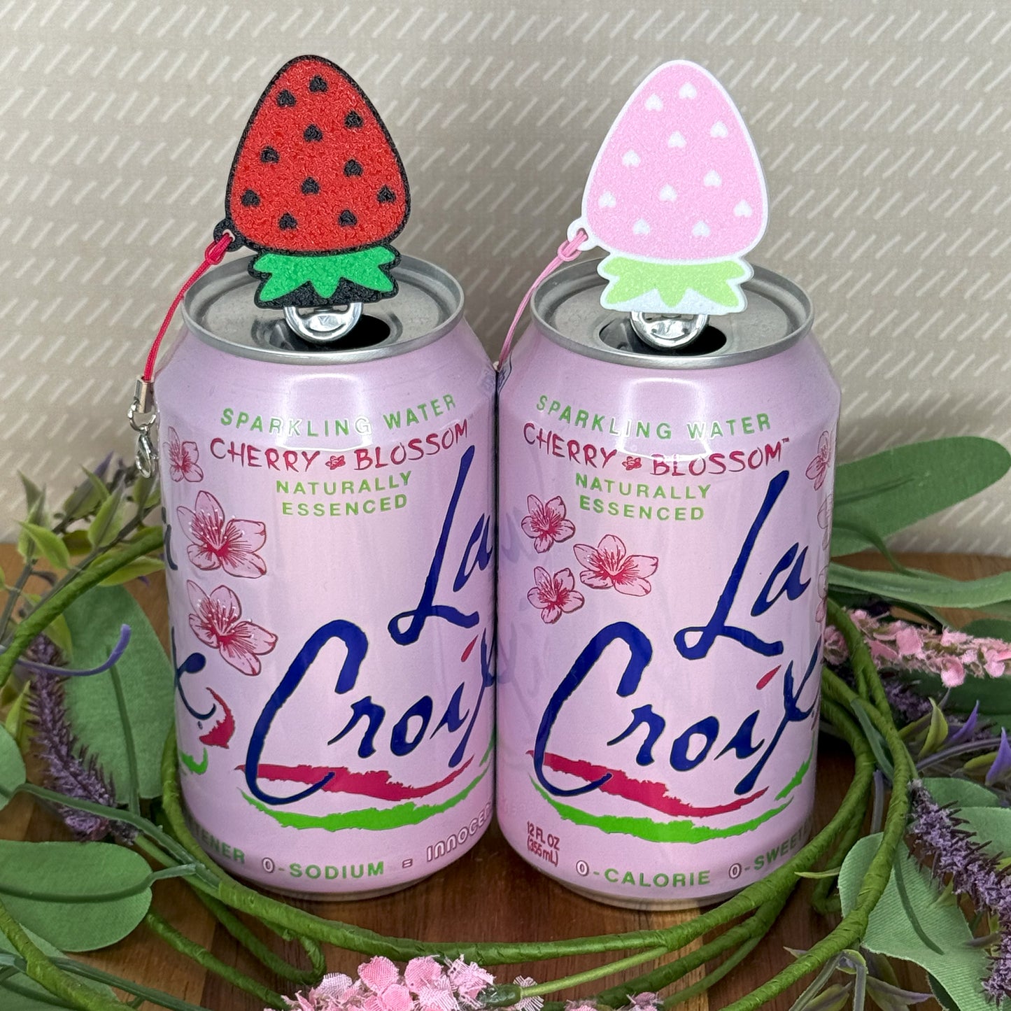 Two La Croix cherry blossom sparkling water cans with strawberry Tab Buddies on a decorative stand.