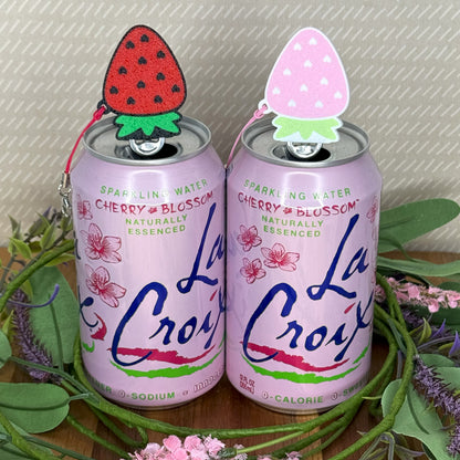 Two La Croix cherry blossom sparkling water cans with strawberry Tab Buddies on a decorative stand.