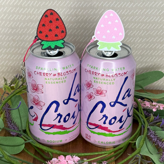 Two La Croix cherry blossom sparkling water cans with strawberry Tab Buddies on a decorative stand.