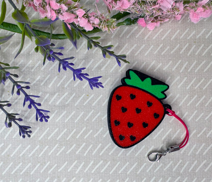 Strawberry-shaped red Tab Buddy keychain with a keyring strap on a beige background with flowers.