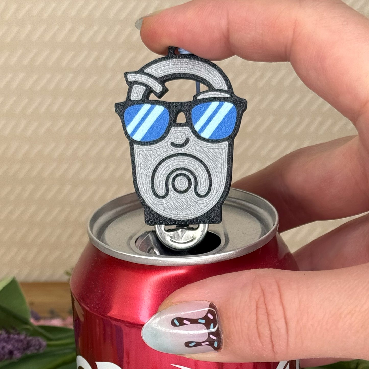 Person holding a can with an OG tab  Tab Buddy shaped like a tab with sunglasses.