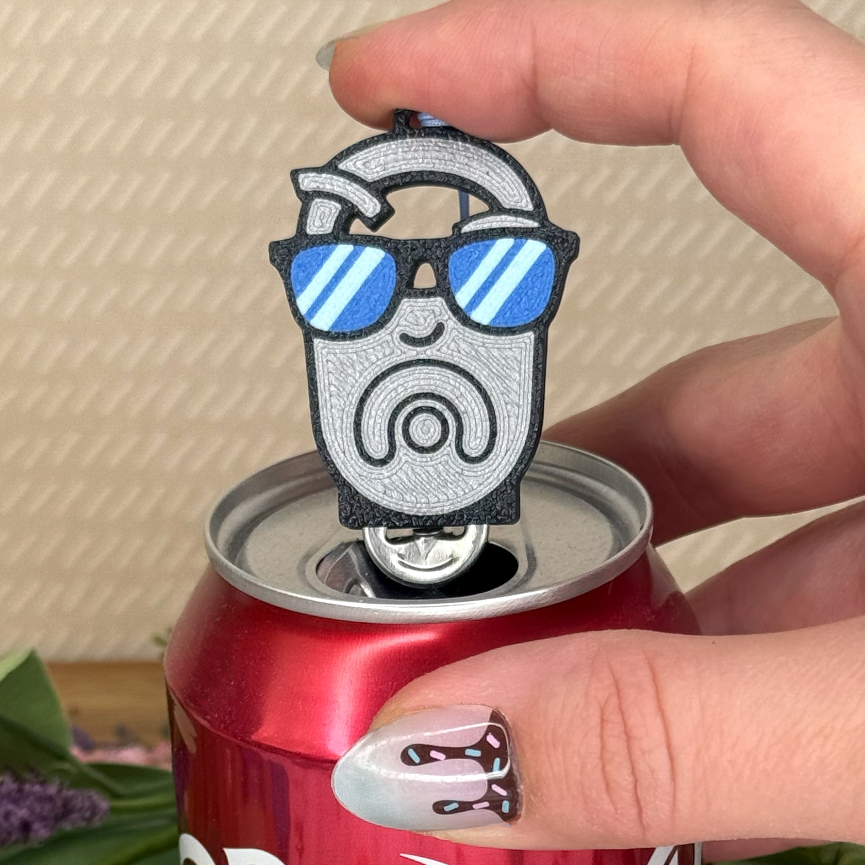 Person holding a can with an OG tab  Tab Buddy shaped like a tab with sunglasses.