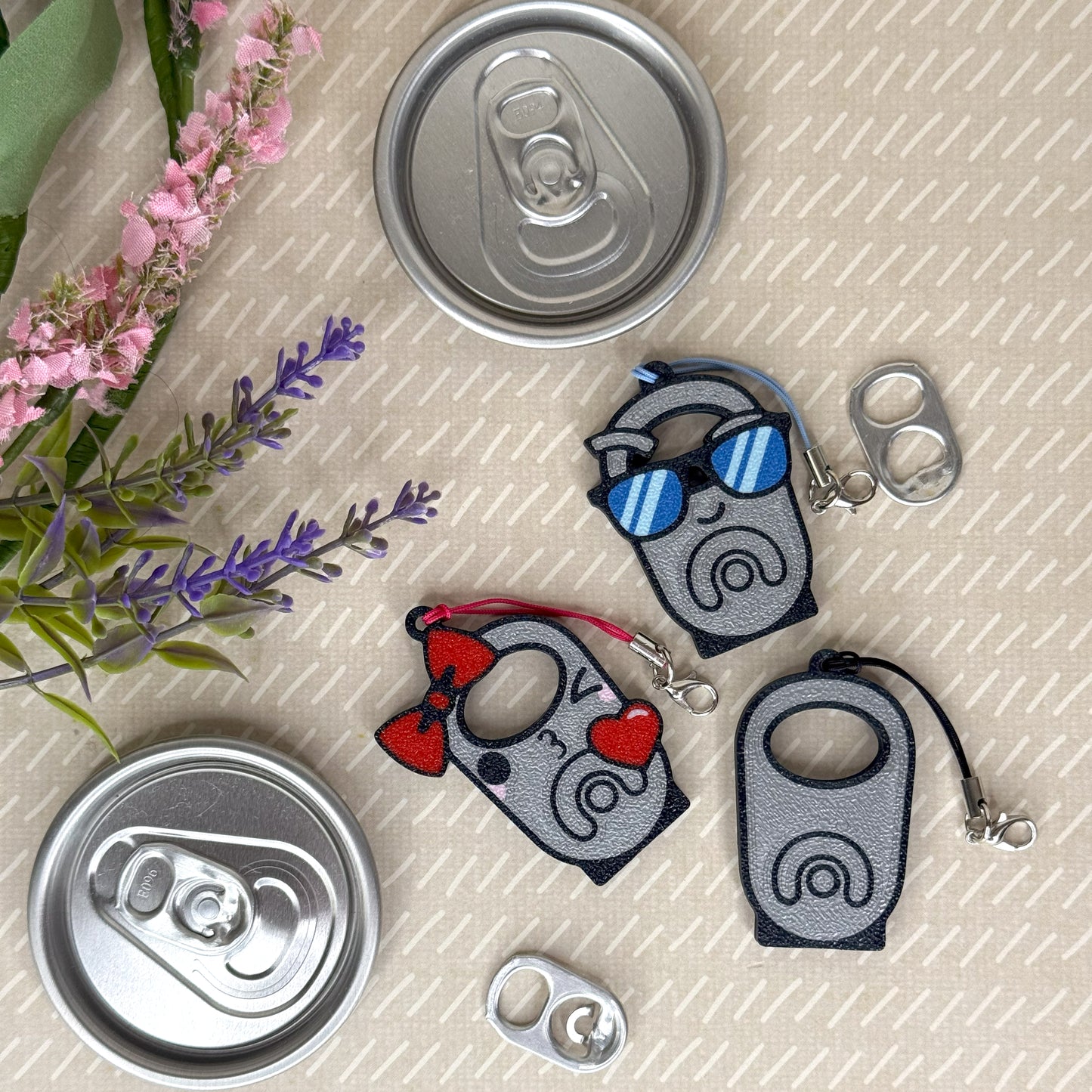 Three Tab Buddies with cartoon designs on a textured surface with flowers and cans.
