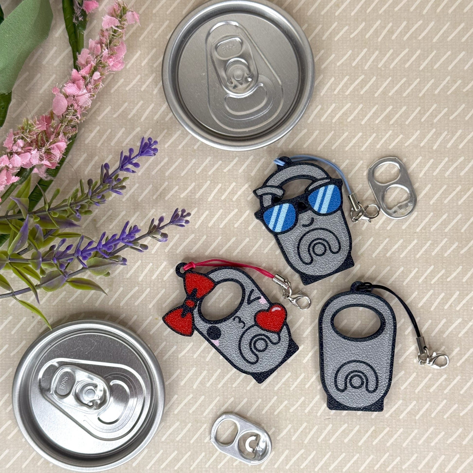 Three Tab Buddies with cartoon designs on a textured surface with flowers and cans.