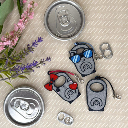Three Tab Buddies with cartoon designs on a textured surface with flowers and cans.