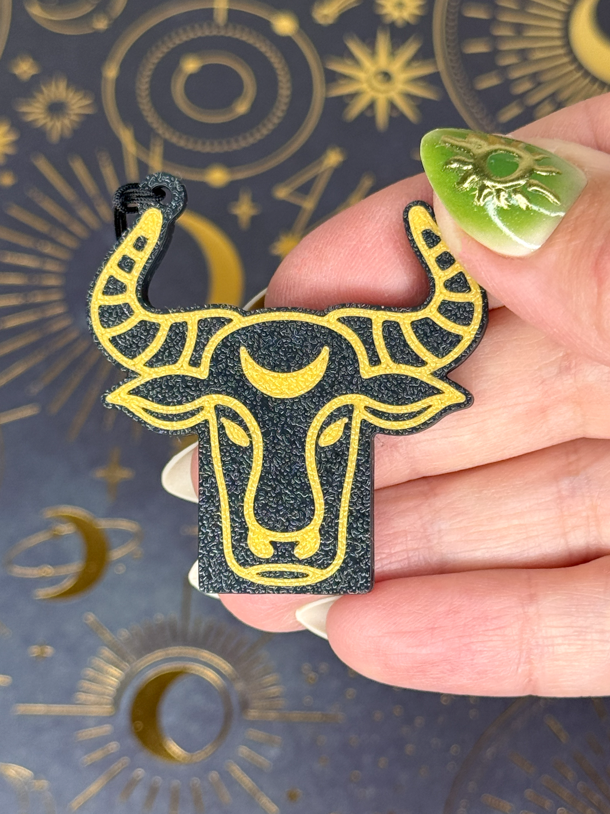 Hand holding a black and gold Taurus zodiac Tab Buddy against a dark background with celestial designs.
