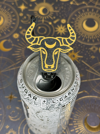 Tab Buddy can opener with gold Taurus bull design on a can against an ornate background