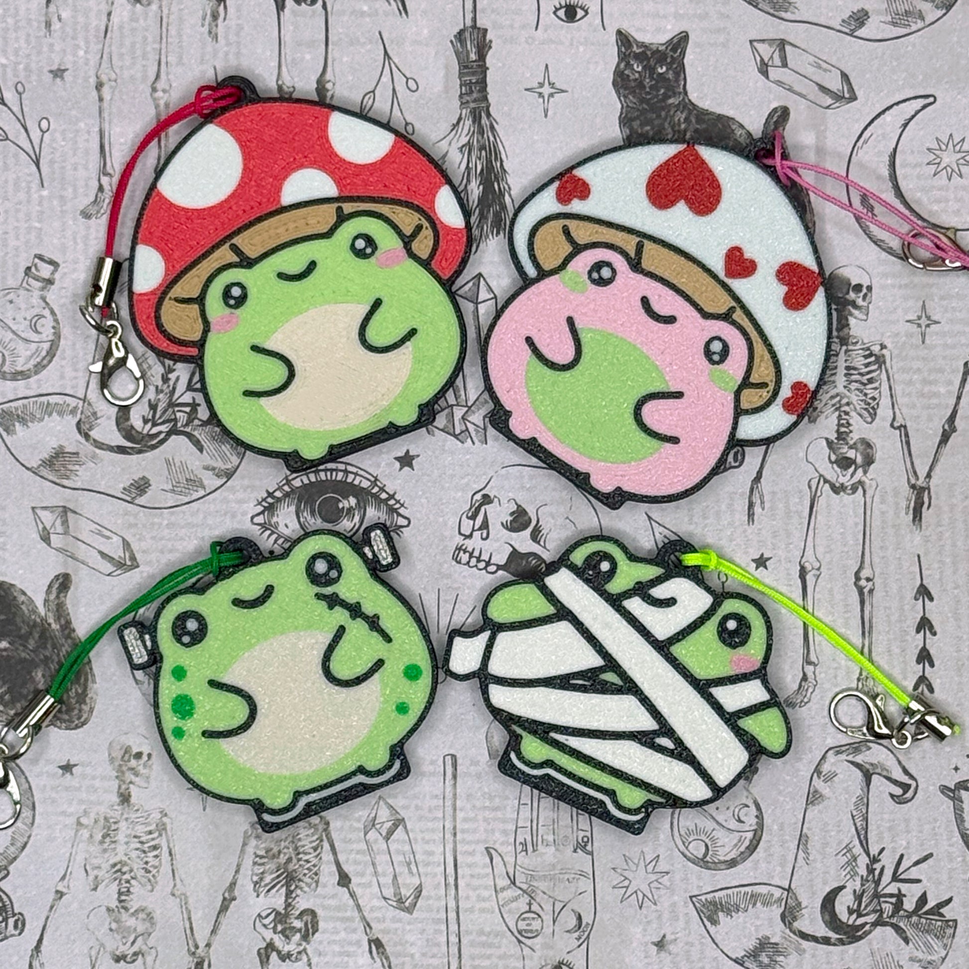 Set of four cartoon-style Tab Buddy frog keychains with different designs on a patterned background.