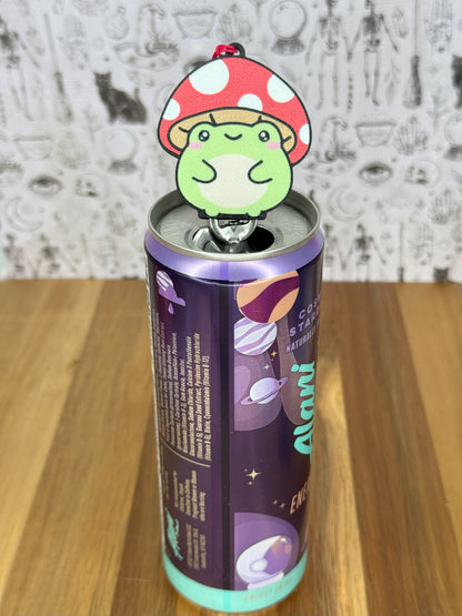 Canned drink with a Tab Buddy of a toadstool frog on top against a textured wall background