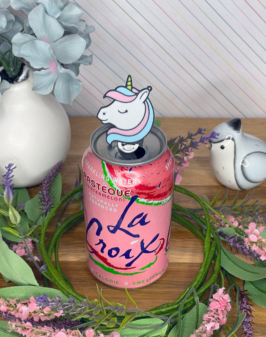 Sparkling water can with a unicorn-themed Tab Buddy surrounded by flowers and decorative items.
