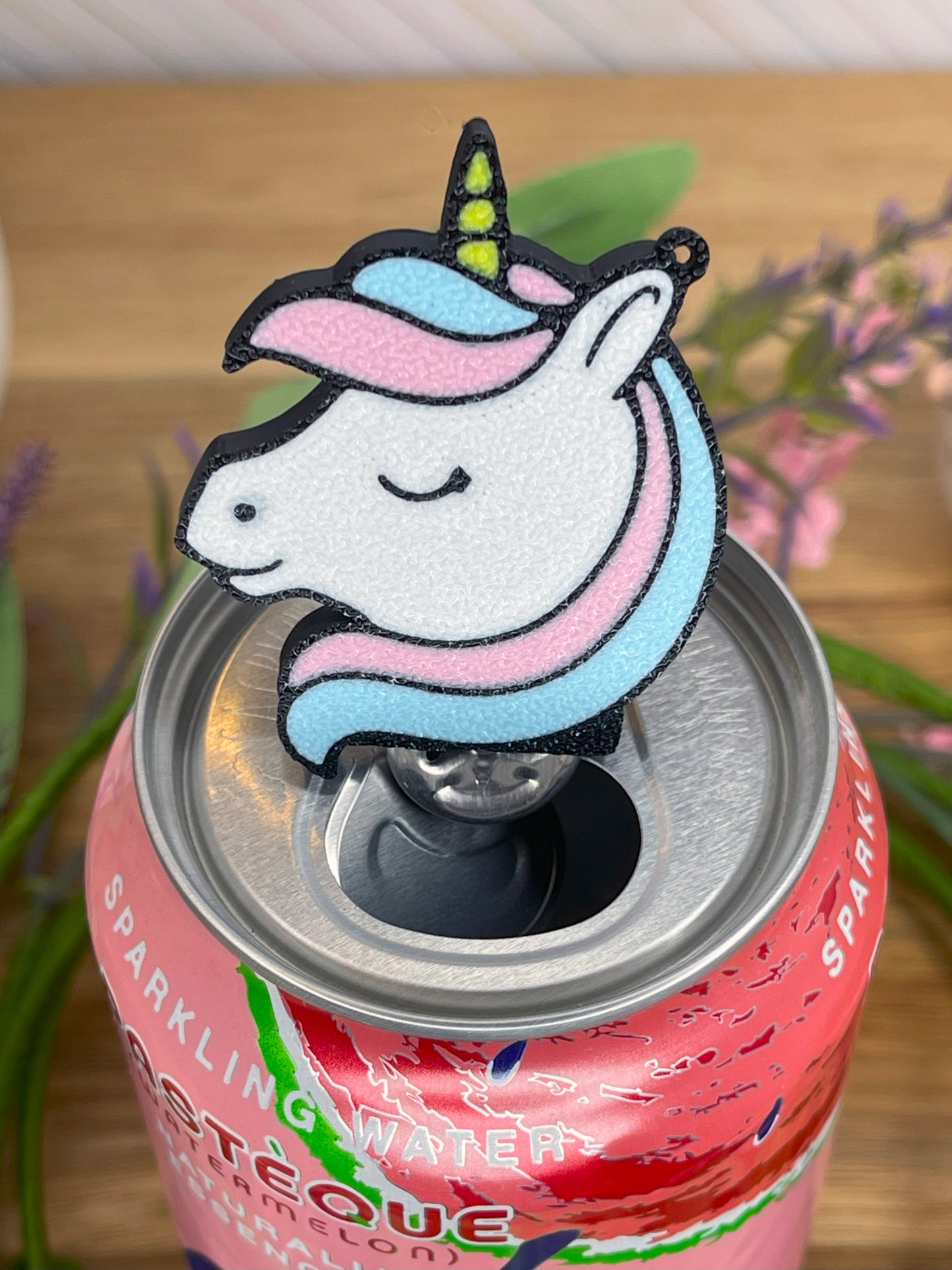 Pink sparkling water can with a unicorn-shaped Tab Buddy on a wooden surface.