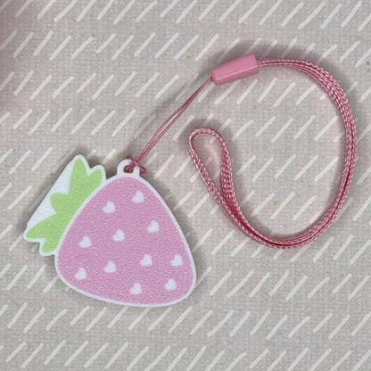 Pink strawberry-shaped Tab Buddy is shown attached to a matching pink wrist strap on a textured beige background