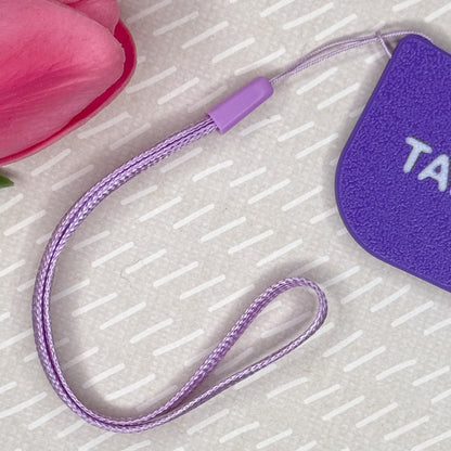 Purple wrist strap is shown attached to matching Tab Buddy XL on a textured surface