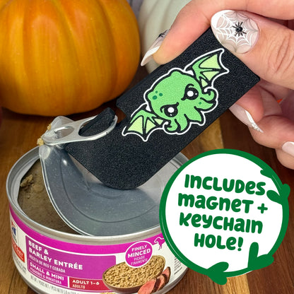 A black and green cthulhu-themed Tab Buddy XL is used to peel back the lid on a can of dog food. Text bubble reads, "Includes magnet + keychain hole!"