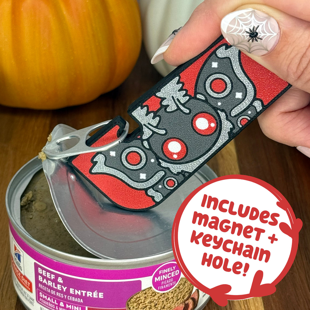 A grey and red Mothman-themed Tab Buddy XL is used to peel back the lid on a can of dog food. Text bubble reads, "Includes magnet + keychain hole!"