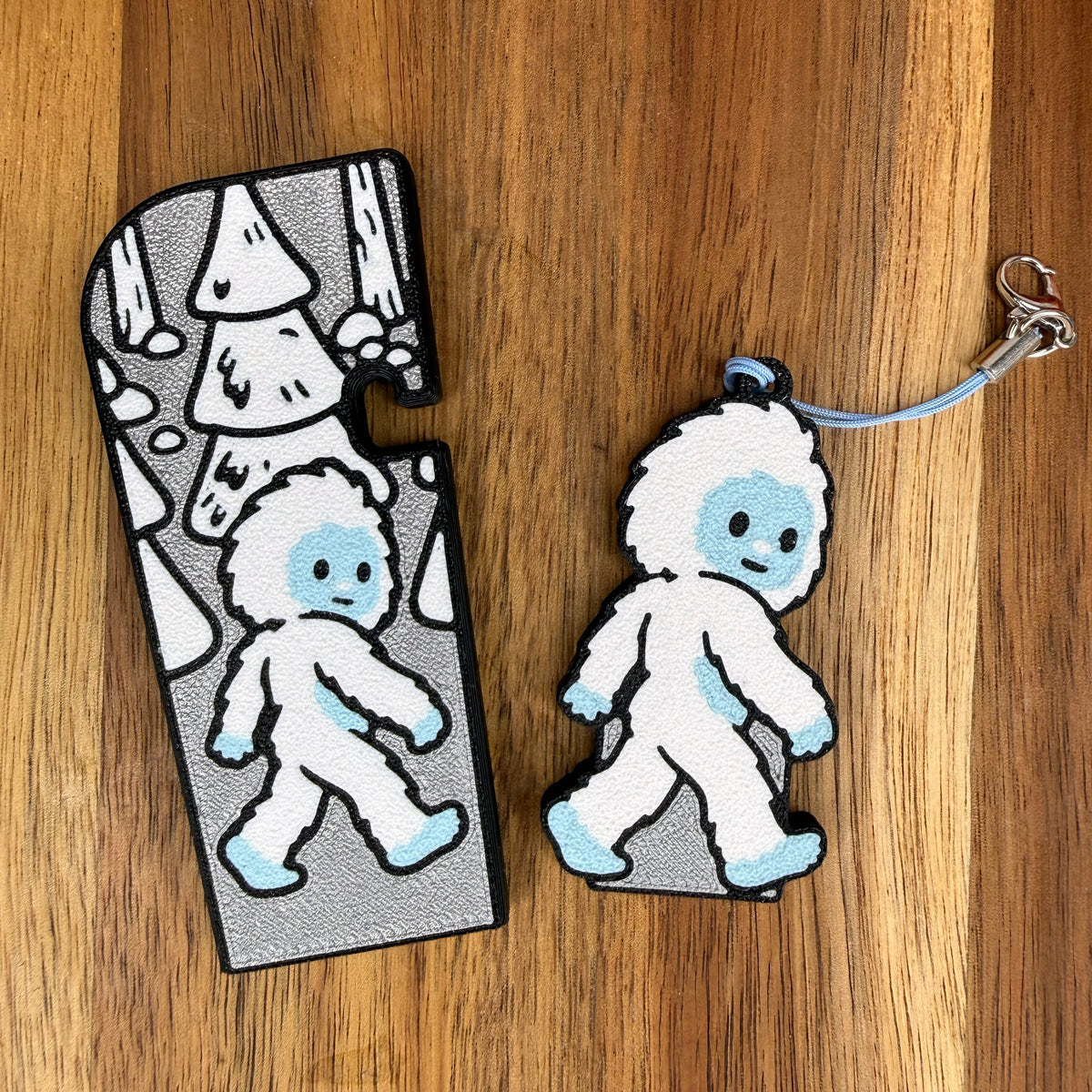 A silver-and-white Yeti-themed Tab Buddy XL and its matching soda-sized Tab Buddy with keychain strap rest on a wooden surface.
