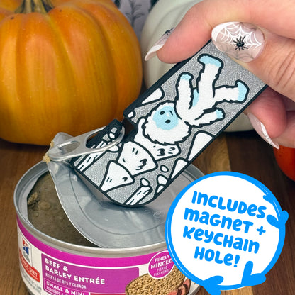 A silver and white Yeti-themed Tab Buddy XL is used to peel back the lid on a can of dog food. Text bubble reads, "Includes magnet + keychain hole!"