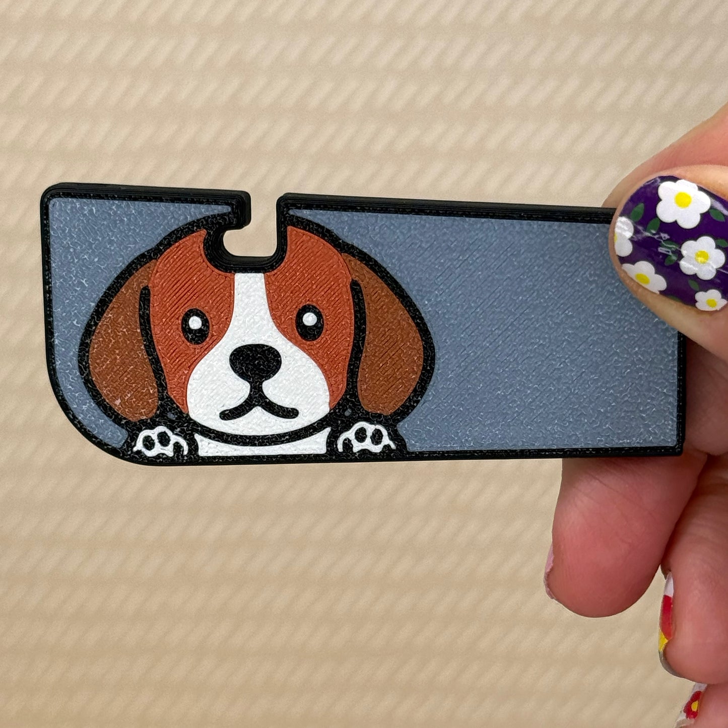 Hand holding a Tab Buddy XL with a cute Beagle dog design and grey background on its surface. A tan surface is in the background of the photo.