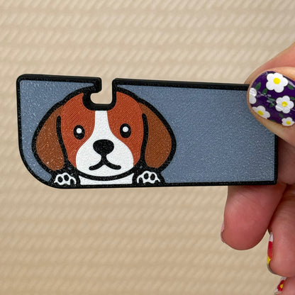 Hand holding a Tab Buddy XL with a cute Beagle dog design and grey background on its surface. A tan surface is in the background of the photo.