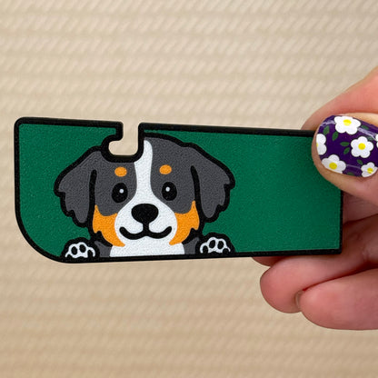 Hand holding a Tab Buddy XL with a cute Bernese Mountain Dog design and green background on its surface. A tan surface is in the background of the photo.