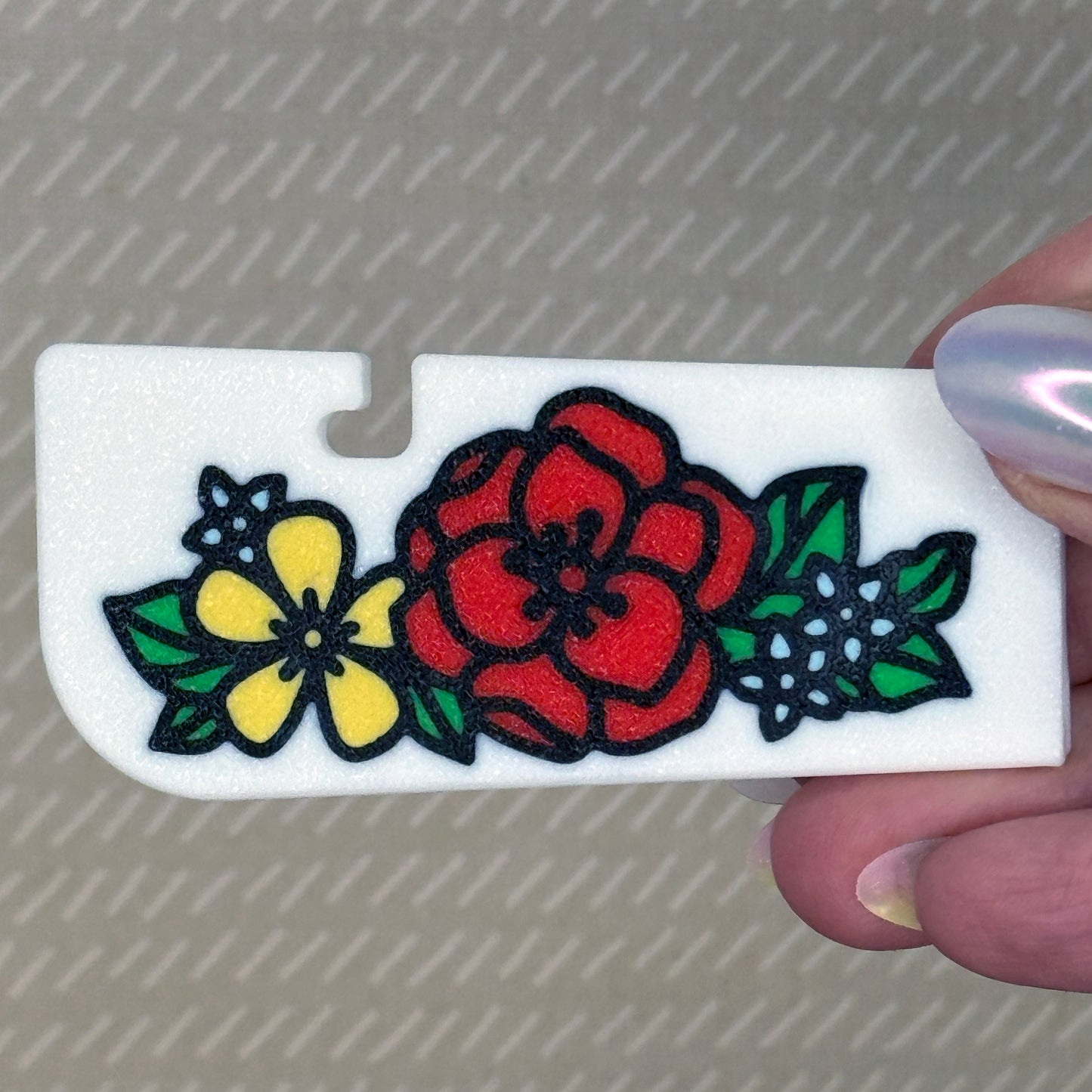 White Tab Buddy XL with Floral design of winter flowers in red, yellow and light blue is held by a manicured hand with a beige background.