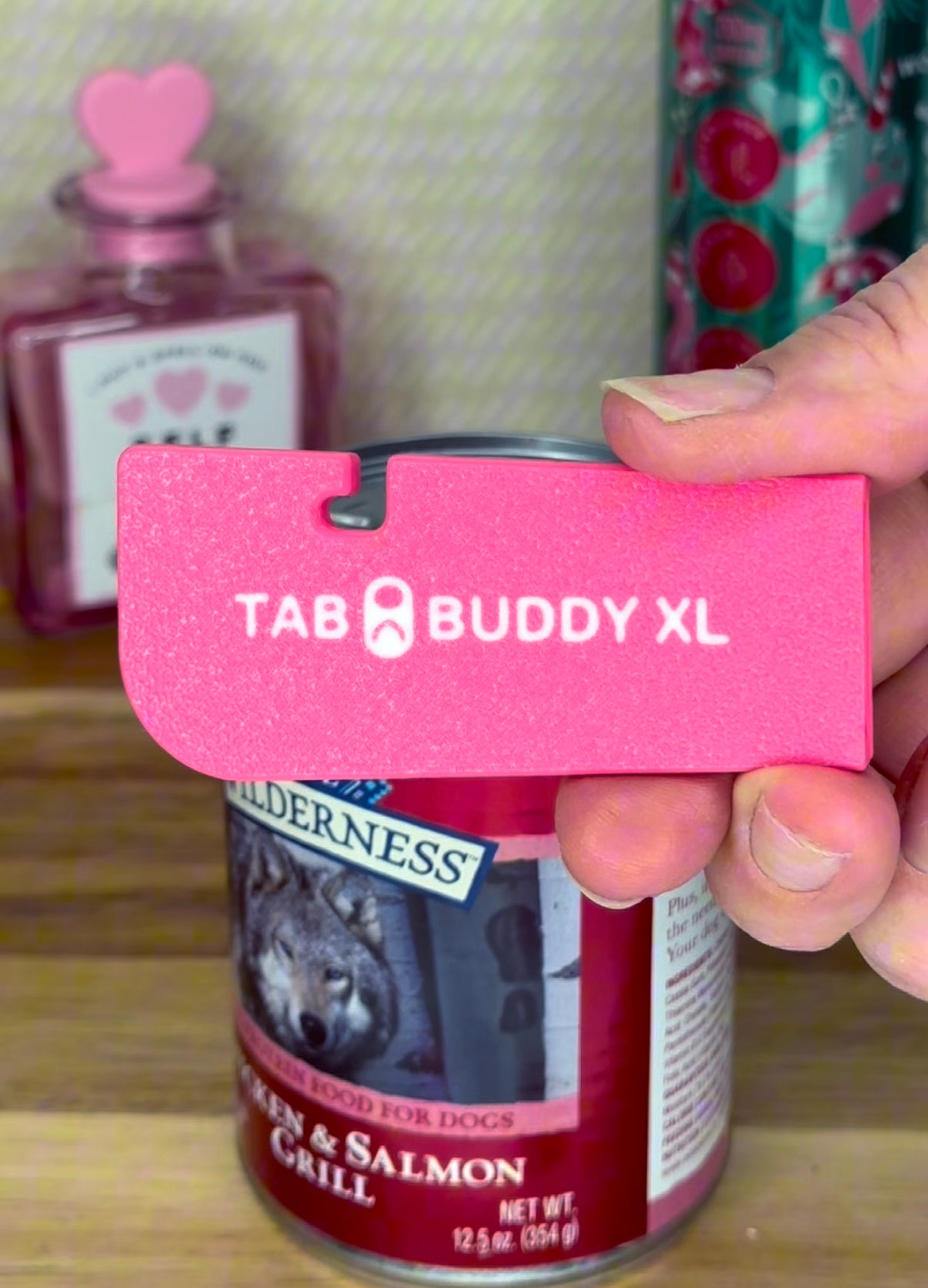 Person holding a bright pink 'Tab Buddy XL' can opener in front of a can of dog food.