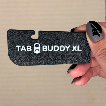 Hand holding a black 'TAB BUDDY XL' product against a beige background