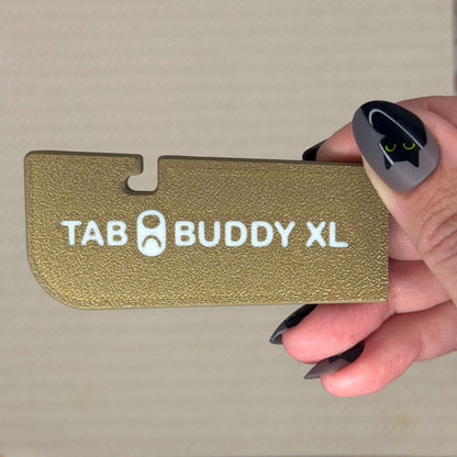 Hand holding a bronze color 'TAB BUDDY XL' product against a neutral background