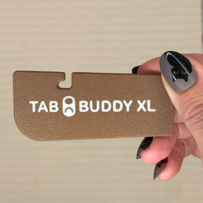 Hand holding a  chocolate brown 'TAB BUDDY XL' product against a beige background