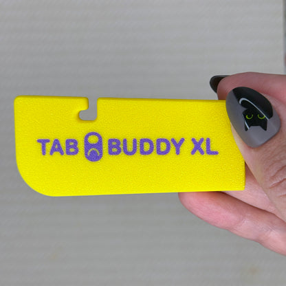 Berry Lemon Yellow 'TAB BUDDY XL' product held by a hand with black nail polish against a gray background