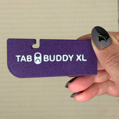 Plum purple 'TAB BUDDY XL' product held by a hand with gray nail polish against a beige background