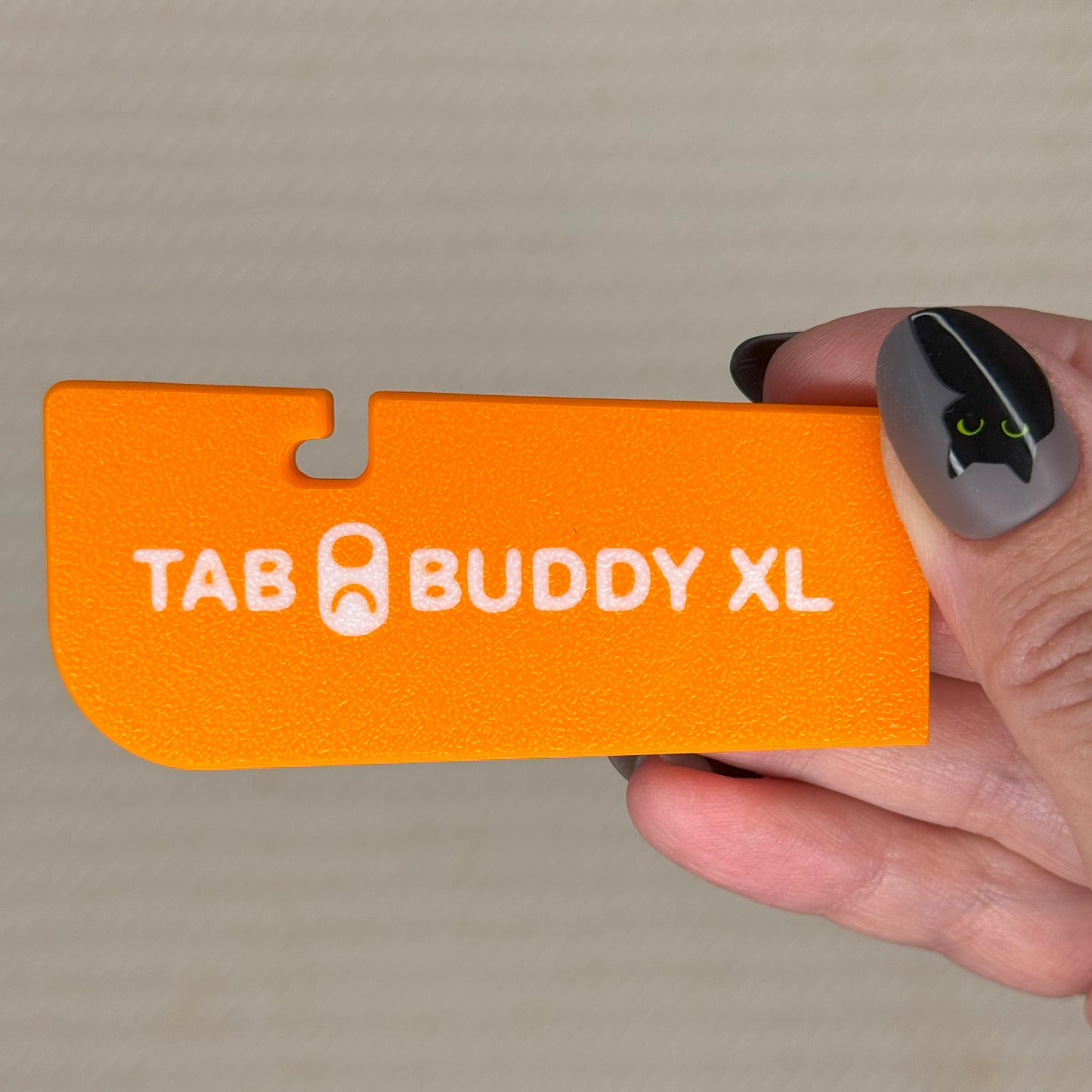 Orange 'Tab Buddy XL' product held by a hand against a neutral background