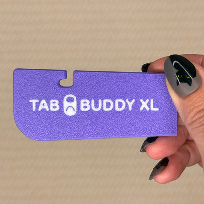 Purple 'TAB BUDDY XL' product held by a hand on a beige background