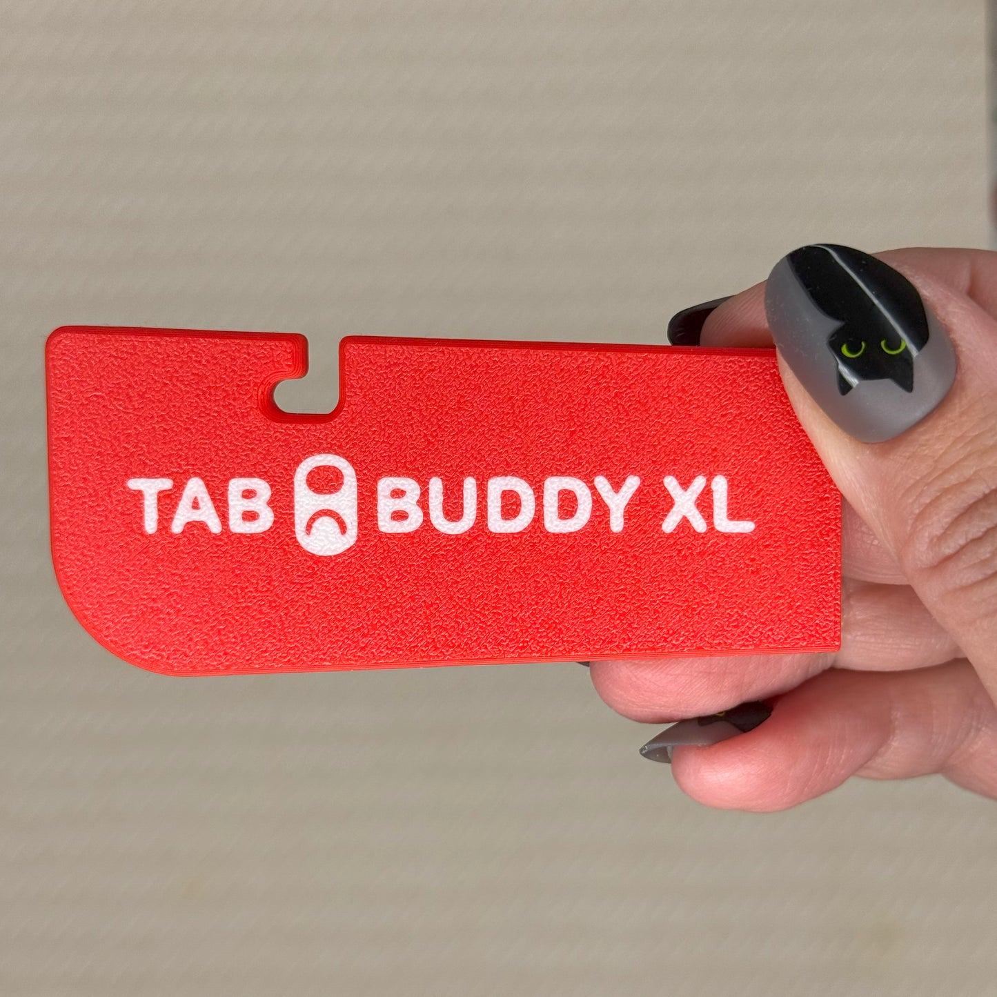 Red 'TAB BUDDY XL' product held by a hand against a neutral background