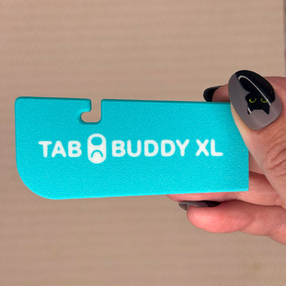 Turquoise 'TAB BUDDY XL' product held by a hand against a beige background