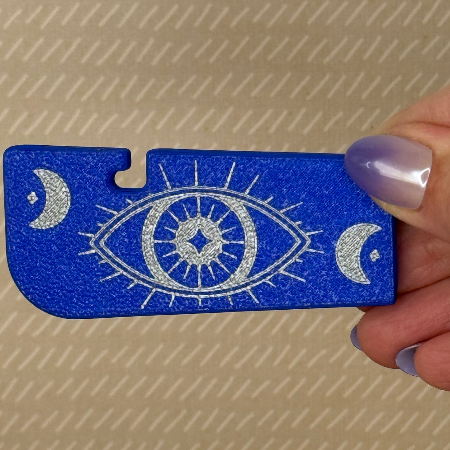Blue Tab Buddy XL with silver eye design held by a hand against a beige background