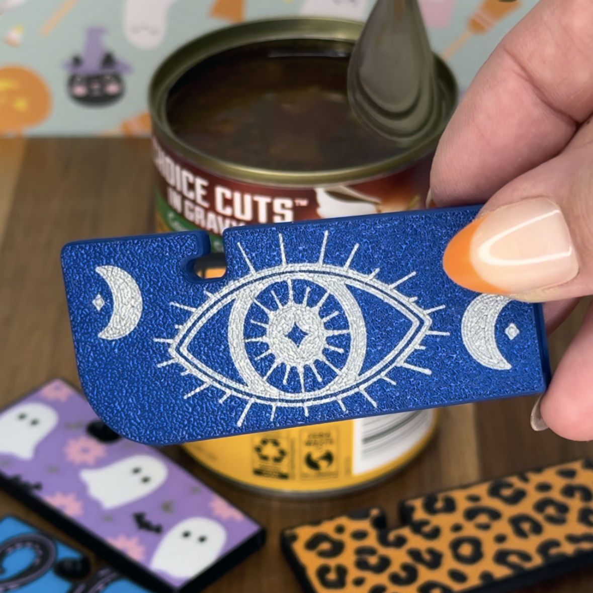 Blue Tab Buddy XL with eye design held by a hand, with a can  in the background.