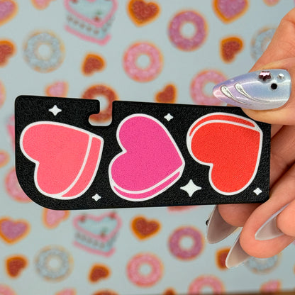 Black Tab Buddy XL with pink and red heart design held by a hand with a colorful background.
