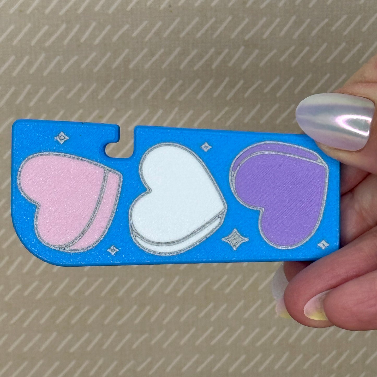 Blue Tab Buddy XL with pink, white, and purple heart shapes held by a hand against a textured background
