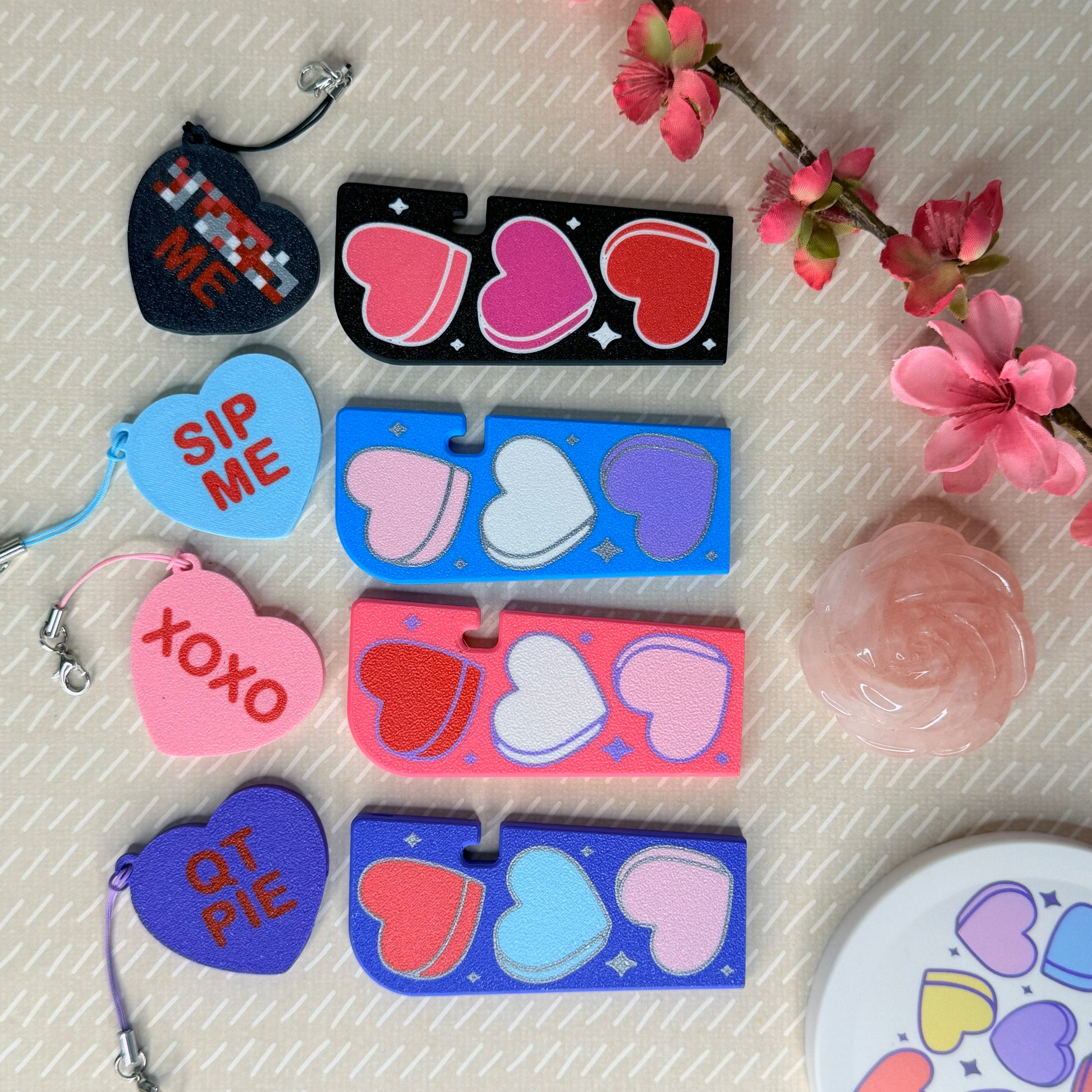 Collection of heart-themed Tab Buddies on a textured surface with flowers.
