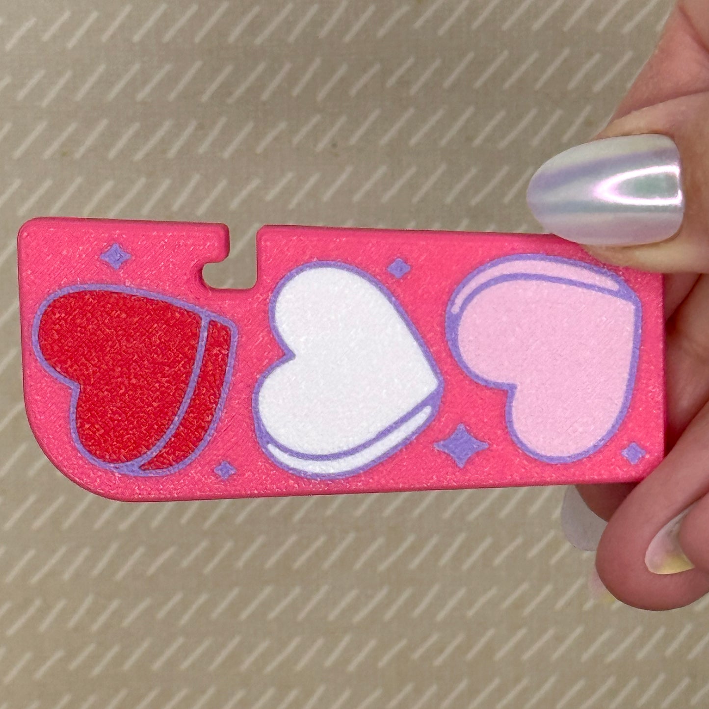 Bright pink Tab Buddy XL with light pink, white, and red heart shapes held by a hand against a textured background