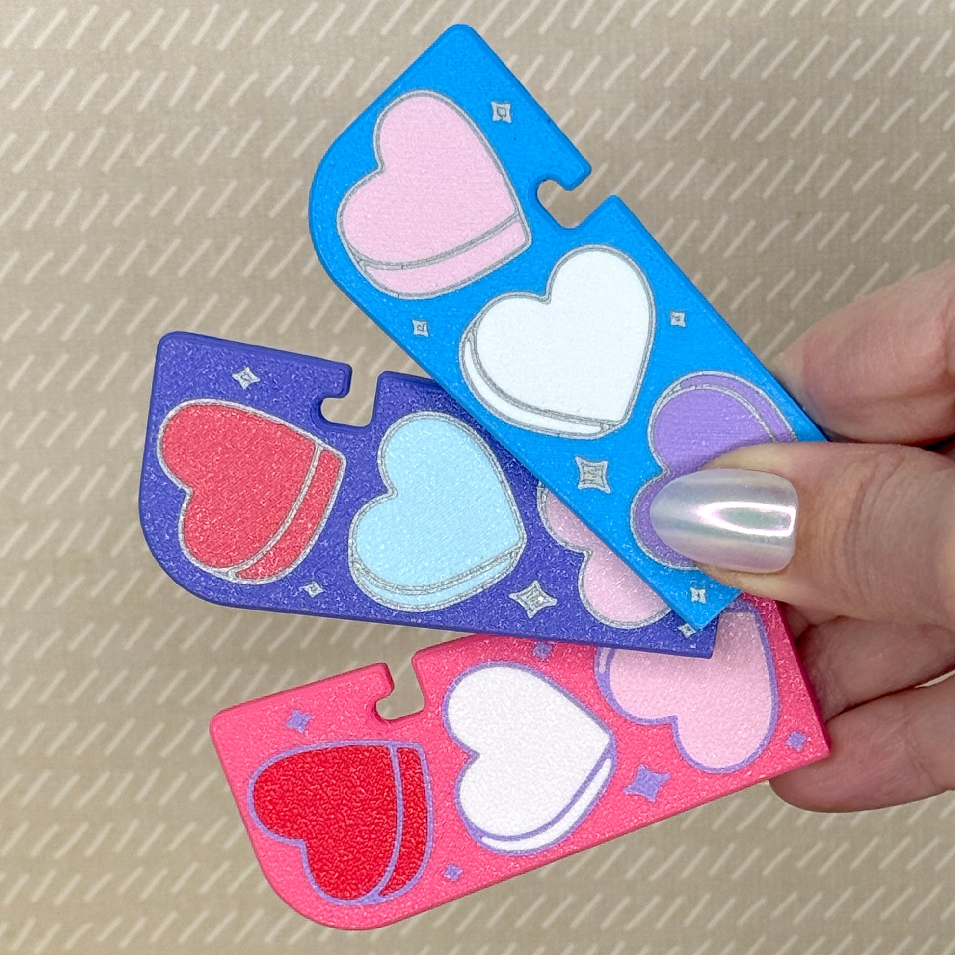 Three Tab Buddy XLs with Candy Hearts design are held in hand. One has a blue background, one purple, and one pink.