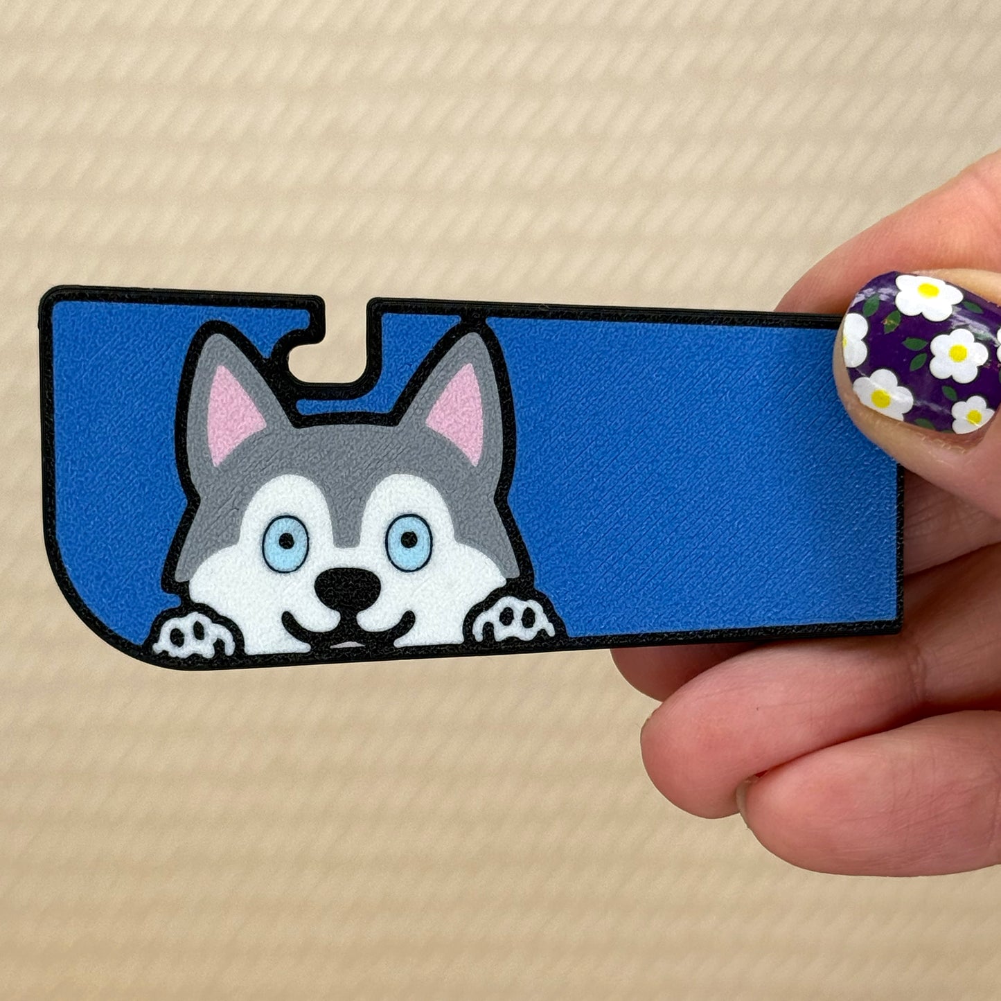 Hand holding a Tab Buddy XL with a cute grey Husky dog design and blue background on its surface. A tan surface is in the background of the photo.