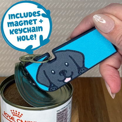 A Black Lab-inspired Tab Buddy XL is used to peel back the lid of a can of dog food. Descriptive text reads "Includes Magnet + Keychain Hole!"