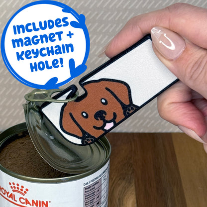 A Chocolate Lab-inspired Tab Buddy XL is used to peel back the lid of a can of dog food. Descriptive text reads "Includes Magnet + Keychain Hole!"